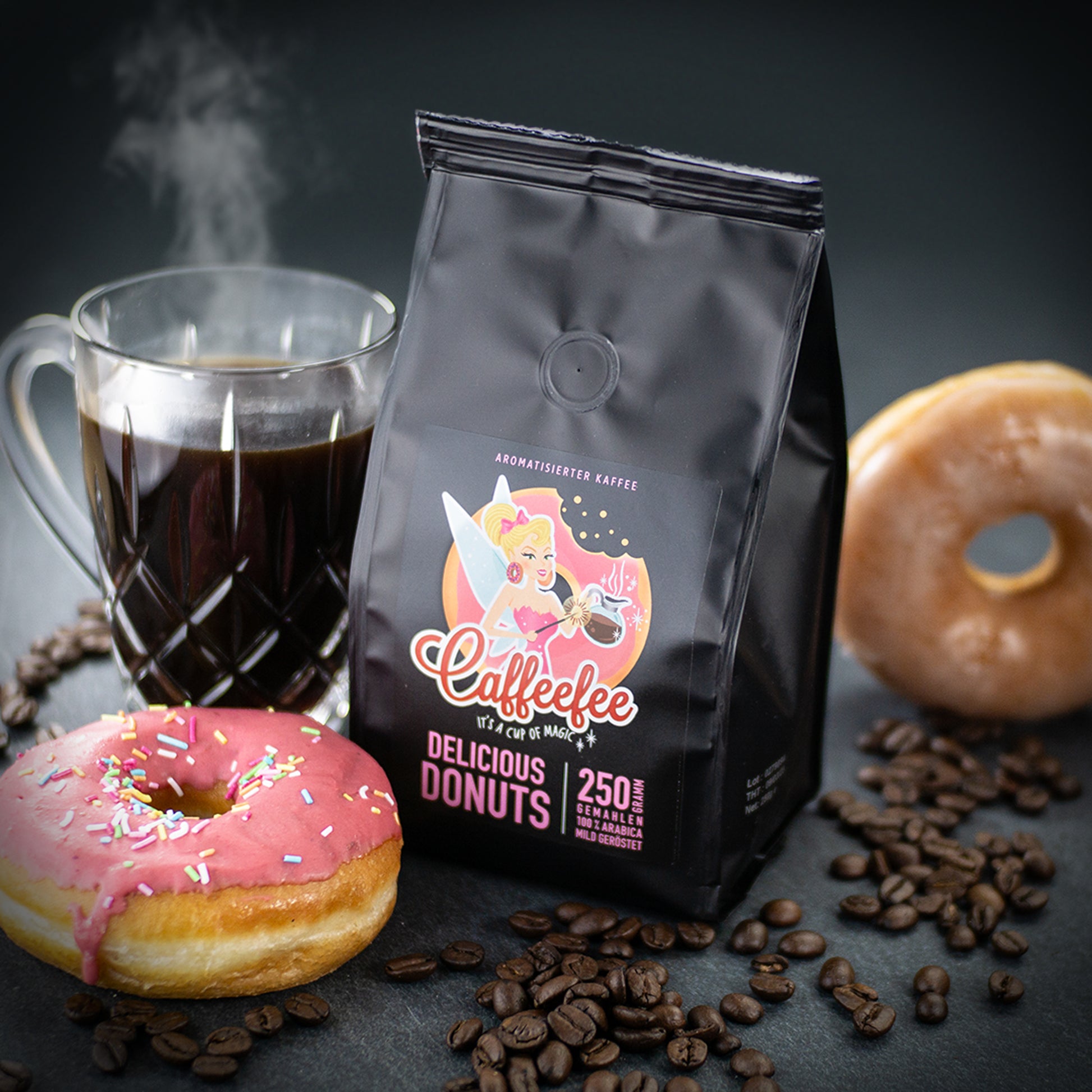 Abbildung Caffeefee Packung mit zwei Donuts und Kaffeetasse mit heißem Kaffee darin. Kaffeebohnen liegen drum herum.